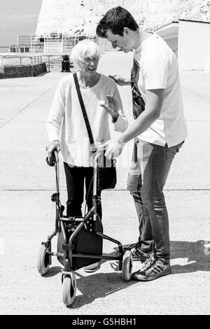 An Elderly Disabled Woman Using A Rollator Walking Aid Helped By Her Grandson, Brighton, Sussex, UK Stock Photo