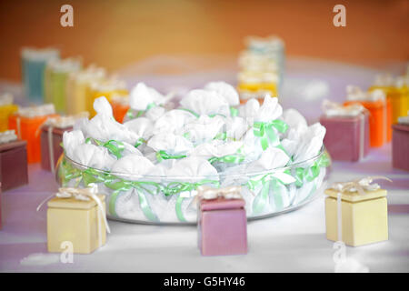 Assorted party favors displayed on a table with colorful gift boxes tied with bows and a bowl of little bags tied with green rib Stock Photo