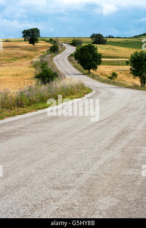 Deserted winding country road leading to low hills through open farmland and fields on a sunny day Stock Photo