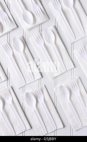 Top view of white napkins with white plastic forks and spoons on a white table. Vertical format. Stock Photo