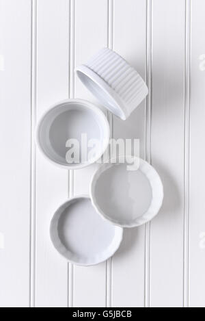 White on white still life of a group of ramekins arranged on a table. The bowls are empty in vertical format. Stock Photo