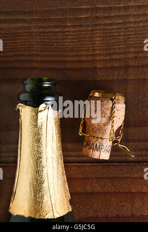 Top view of an opened Champagne bottle next to a cork and cage. Vertical format on dark wood background, with copy space. Stock Photo