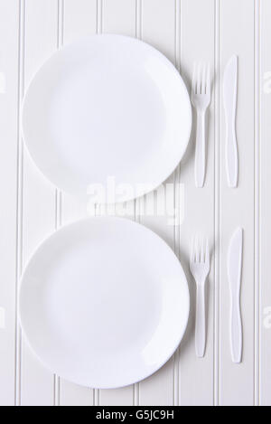 Top view of an all white place setting. White plates and plastic utensils on a white background. Stock Photo