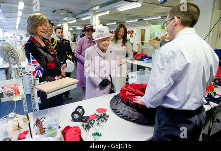 Queen Elizabeth II watches an employee of The Poppy Factory making the red emblem of the British Legion's annual poppy appeal during a visit to the company headquarters in Richmond, London. Stock Photo