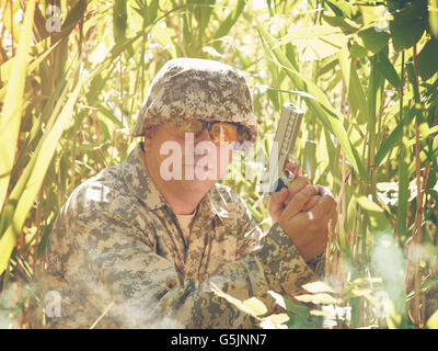 An army soldier man is holding a hand gun in the forest with tall grass outside for a defense, safety or combat war concept. Stock Photo