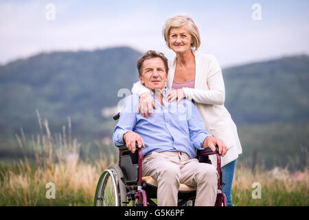 Senior woman pushing man in wheelchair, green autumn nature Stock Photo