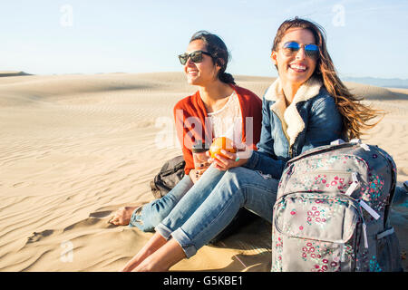 Mixed race women sitting on sand dunes Stock Photo