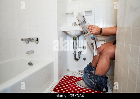 Mixed race man reading newspaper on toilet Stock Photo