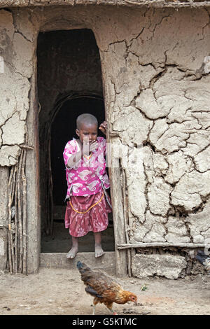 Young Masai child standing in the doorway of a mud hut in the Masai village, Kenya, Africa.