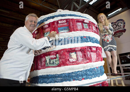 To celebrate 100 years of Belling, television chef Brian Turner helps specialist cake maker Connie Viney add the finishing touches to her 6ft tall cake which illustrating major events of the last decade, at the BBC Good Food Show Winter at the NEC in Birmingham. Stock Photo