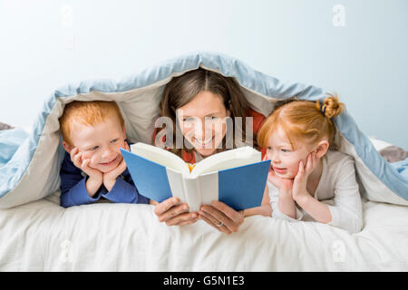 Caucasian mother and children reading book in bed Stock Photo