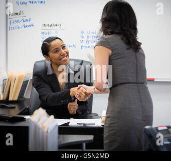 Businesswomen shaking hands in office Stock Photo