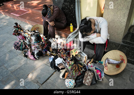Two young women who sell tourist gifts, rest on the steps of a building in the Old District of Hanoi, Hoan Kiem, Vietnam.