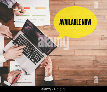 BUSINESS TEAM WORKING IN OFFICE WITH AVAILABLE NOW SPEECH BUBBLE ON DESK Stock Photo