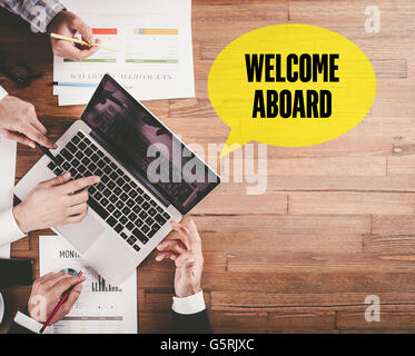 BUSINESS TEAM WORKING IN OFFICE WITH WELCOME ABOARD SPEECH BUBBLE ON DESK Stock Photo