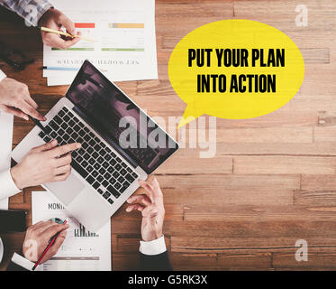 BUSINESS TEAM WORKING IN OFFICE WITH PUT YOUR PLAN INTO ACTION SPEECH BUBBLE ON DESK Stock Photo