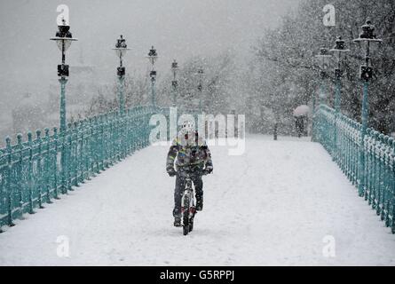 A man rides his bike through the snow across the Spa Bridge in Scarborough as snow hit parts of England today with up to 4in (10cm) expected to fall in some areas, prompting fears of travel chaos. Stock Photo