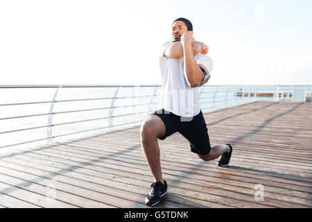 Serious african american young sportsman stretching legs and arms at the sunrise Stock Photo