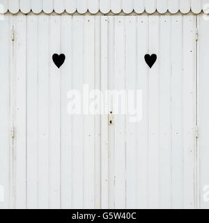 Detail of white wooden beach hut with two carved hearts in the doors. Stock Photo