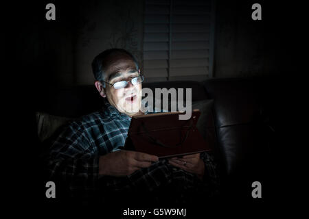 Yawning middle aged man wearing pajamas reading tablet at night in bed with copy space Stock Photo