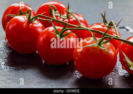 Small cherry tomatoes on black stone background. Closeup, selective focus. Stock Photo