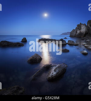Colorful night landscape with full moon, lunar path and rocks in summer. Mountain landscape at the sea Stock Photo
