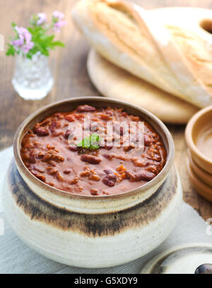 Top view of chilli con cane Shallow depth of field shot on a wooden table in a place setting with bread and plates ,window light