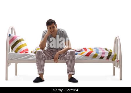 Depressed young man sitting on a bed and contemplating isolated on white background Stock Photo