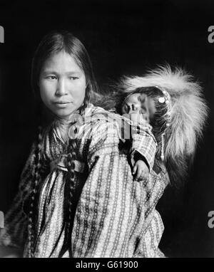 Inuit woman, wearing traditional clothes, with a papoose on her back in Arctic Alaska. Photo by H G Kaiser, c.1912 Stock Photo