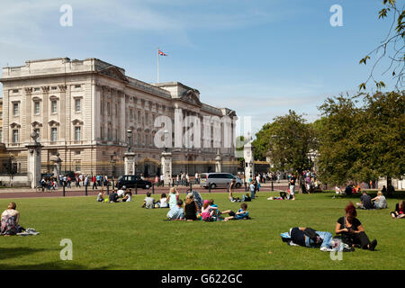 Tourists resting on the grass outside Buckingham Palace, London, England, United Kingdom, Europe Stock Photo