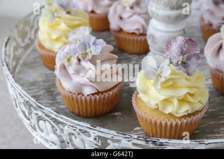 Purple and yellow cupcakes with sugared edible flowers on vintage cake stand Stock Photo