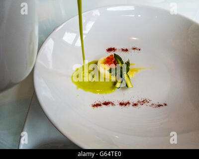 Pouring asparagus soup over quail egg and salmon roe with tiny asparagus during gourmet meal. Stock Photo