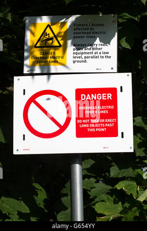 A 'Danger, Overhead Power Cable' public warning sign posted below overhead live cables on the banks of the River Wear, Durham. Stock Photo