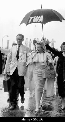 An umbrella is held aloft as Marilyn Monroe and her husband, playwright Arthur Miller walk from a TWA plane on their arrival from New York. Marilyn has come to make the film 'The Sleeping Prince' with Sir Laurance at Pinewood. Stock Photo