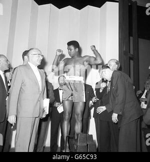 American heavyweight Cassius Clay on the scales during the weigh-in at London Palladium. Clay continued his confident boastings that he will beat British heavyweight champion Henry Cooper in five rounds in their fight at Wembley Stadium tonight. Stock Photo