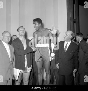 American heavyweight Cassius Clay pretends to be hurt by Henry Cooper's hand shake on the scales during the weigh-in at London Palladium. Clay continued his confident boastings that he will beat British heavyweight champion Henry Cooper in five rounds in their fight at Wembley Stadium tonight. Stock Photo