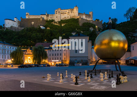 Night view of Kapitelplatz square with golden ball monument named Sphaera and Hohensalzburg Castle behind, Salzburg, Austria Stock Photo