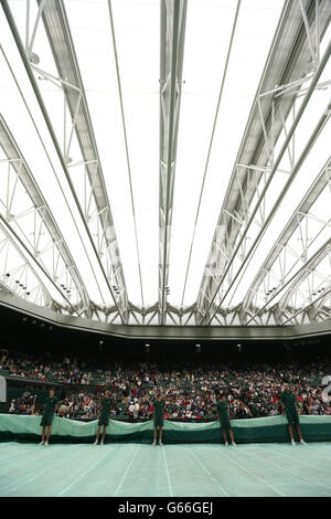 Groundstaff race to put the covers on centre court as rain stops play during the match between Poland's Agnieszka Radwanska and France's Mathilde Johansson during day four of the Wimbledon Championships at The All England Lawn Tennis and Croquet Club, Wimbledon. Stock Photo