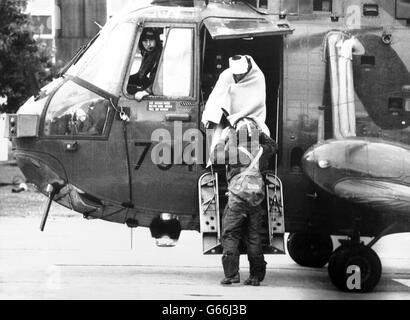 With bandaged head and swathed in a blanket, a survivor of the North Sea oil production platform Piper Alpha is helped from a rescue helicopter at Aberdeen Royal Infirmary. An extensive search for survivors followed on after the disaster, which saw the platform quickly become a raging inferno. Stock Photo