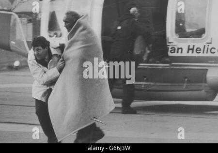 A weary survivor is helped to an ambulance from the rescue helicopter, which landed at Aberdeen Royal Infirmary after the explosion disaster on the North Sea oil production platform Piper Alpha. *Low res scan - hi res scan on request Stock Photo