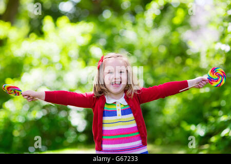 Cute little girl with big colorful lollipop. Child eating sweet candy bar. Sweets for young kids. Summer outdoor fun. Stock Photo