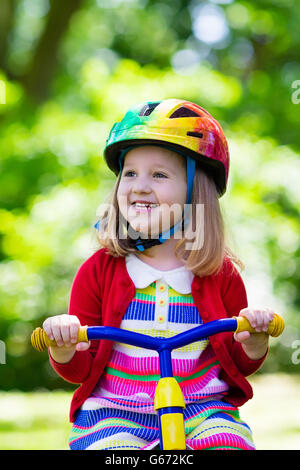 Cute girl wearing safety helmet riding her tricycle in sunny summer park. Kids ride bicycle. First bike for little child Stock Photo