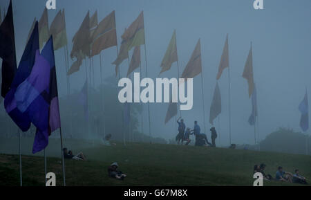 Festival-goers walk through a field of flags at dawn, during the final day of the 2013 Glastonbury Festival of Contemporary Performing Arts at Pilton Farm, Somerset. Stock Photo