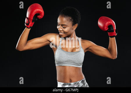 Portrait of a smiling fitness woman standing with boxing gloves in victory pose isolated on a black background Stock Photo