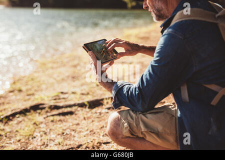 Close up portrait of senior male hiker with backpack using digital tab and looking for location during hike in nature. Mature ma Stock Photo