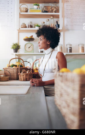 Side portrait of young woman employee standing at juice bar counter. African female fruit juice bar owner. Stock Photo
