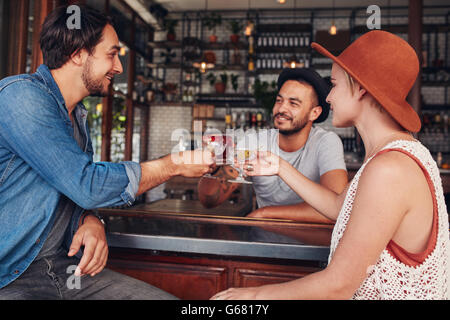 Three young people toasting drinks at cafe. Young men and woman having a glass of drink at bar. Stock Photo