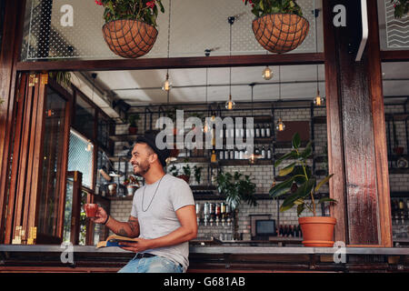 Happy young man drinking coffee and reading book at a cafe. Young guy enjoying a cup of coffee while reading a novel. Stock Photo