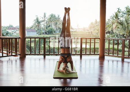 Rear view shot of fitness woman doing the headstand yoga in healthy club. Healthy female doing headstand asana. Sirsasana. Stock Photo