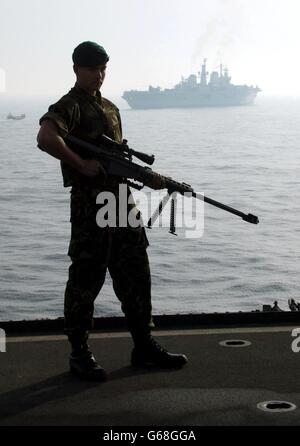 A Royal Marine from 40 Commando stands on the deck of British helicopter carrier HMS Ocean, with the HMS Ark Royal in the background, as they travel through the Persian Gulf. Stock Photo
